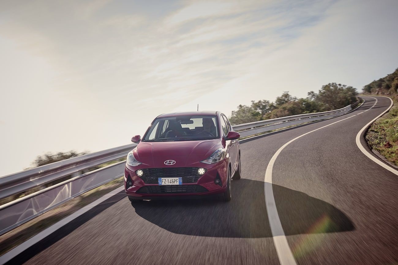 red hyundai i10 driving down a road