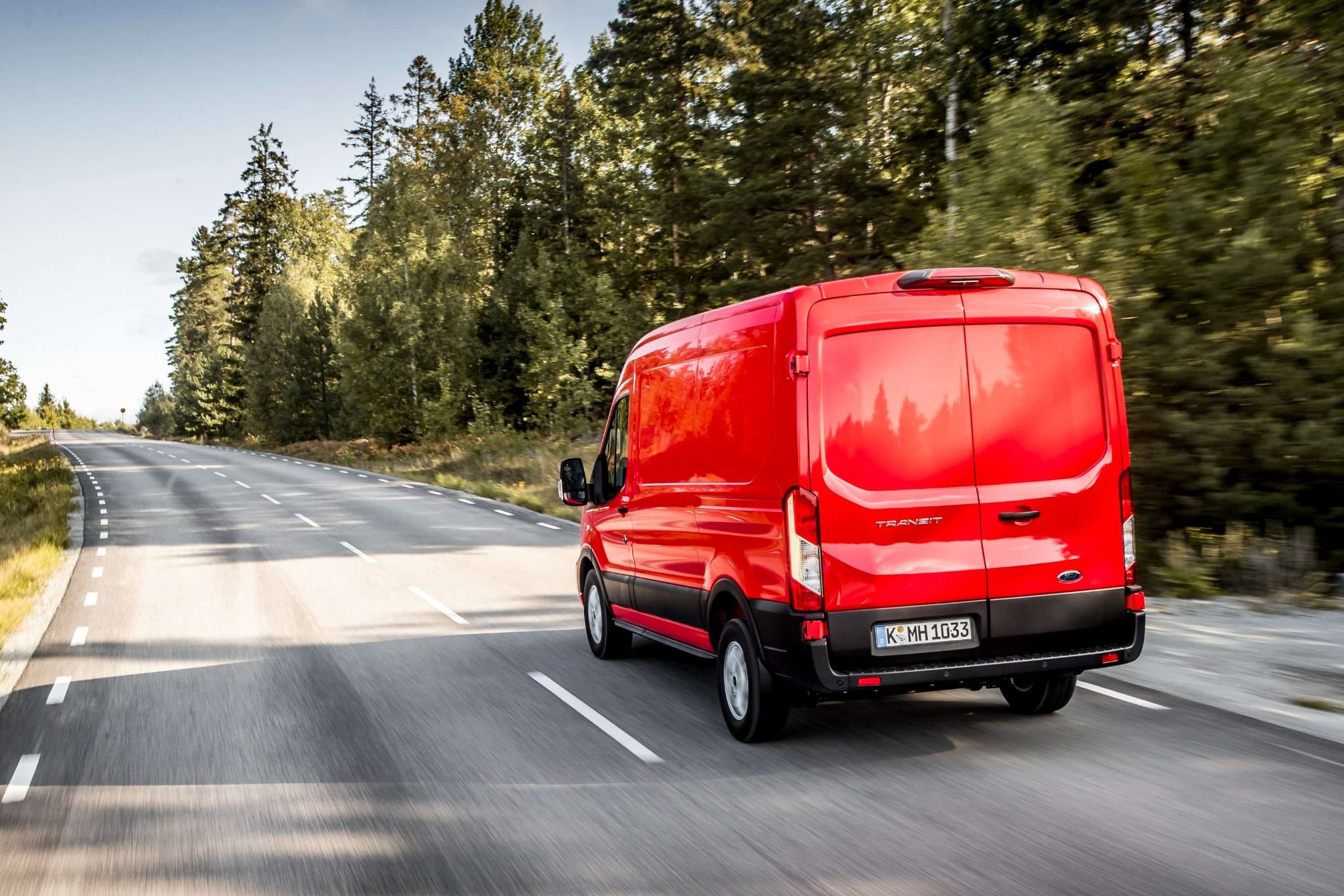 Rear Image of a Ford Transit Van Driving Along a Road Framed by Trees