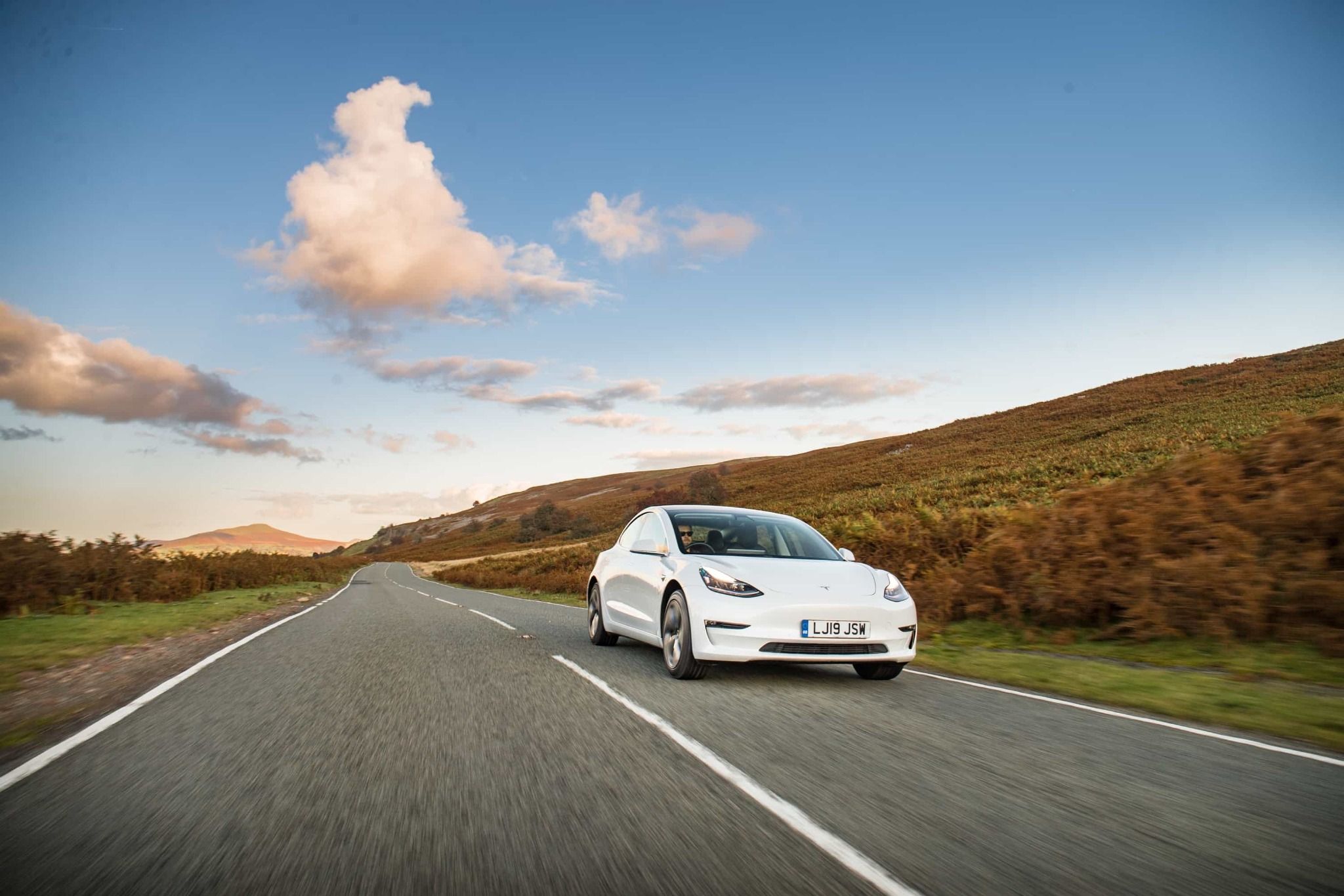 white tesla driving down a country road