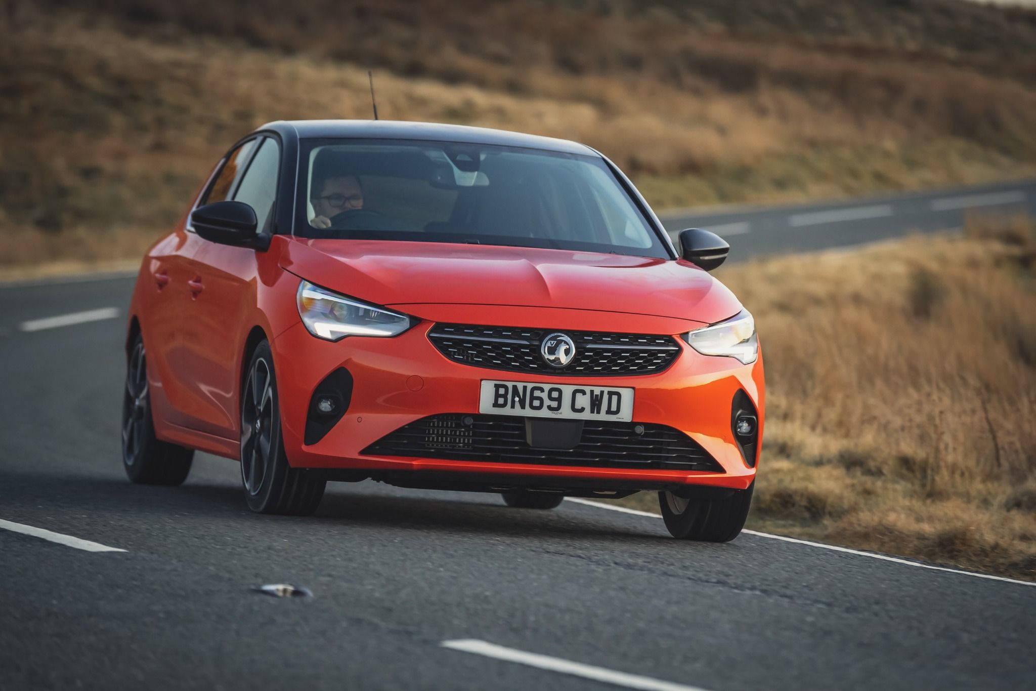 red Vauxhall Corsa driving down a country road