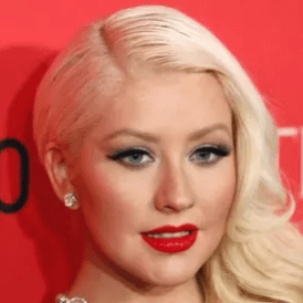 Christina Aguilera with red lipstick smiling at an awards red carpet